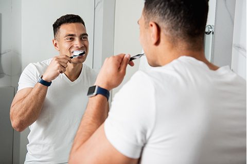 A man standing in front of his bathroom mirror brushing his teeth in Orange