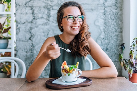 A female sitting down to eat a fruit yogurt cup and smiling in Orange