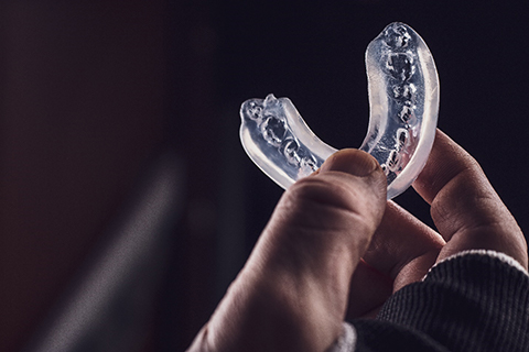 An up-close image of a person holding a customized mouthguard in Orange