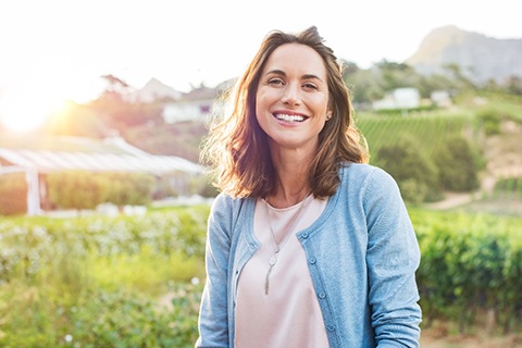 A woman standing in a field and smiling after learning how to prevent dental injuries by her emergency dentist in Orange