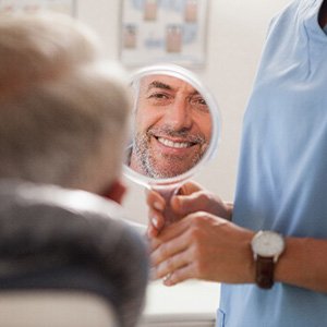 Mature man smiling at reflection in dentist's mirror