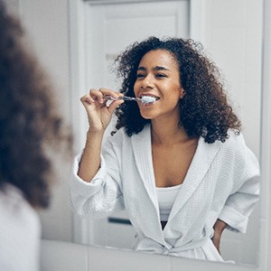 Young woman with curly hair smiling while brushing her teeth