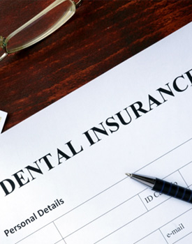 Dental insurance paperwork, dental X-rays, glasses, and money sitting on a wooden table 