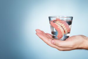 Set of dentures in a glass of liquid held by a flat hand