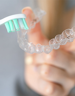 Patient using toothbrush to clean aligner