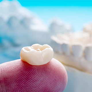 Dental crown held on finger.